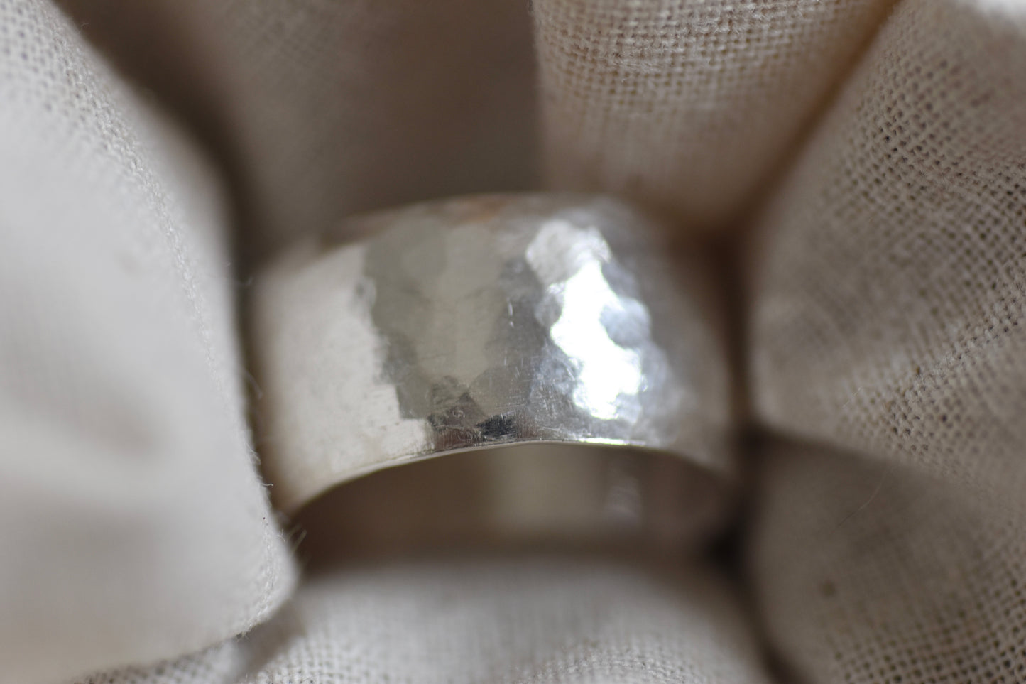 A hammered sterling silver band ring nestled in soft, textured off-white fabric.