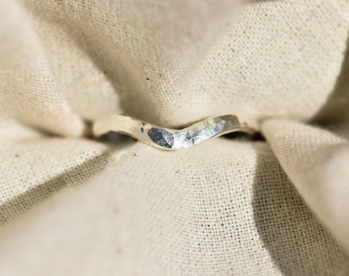 A hammered silver band ring resting on a textured beige linen fabric background.