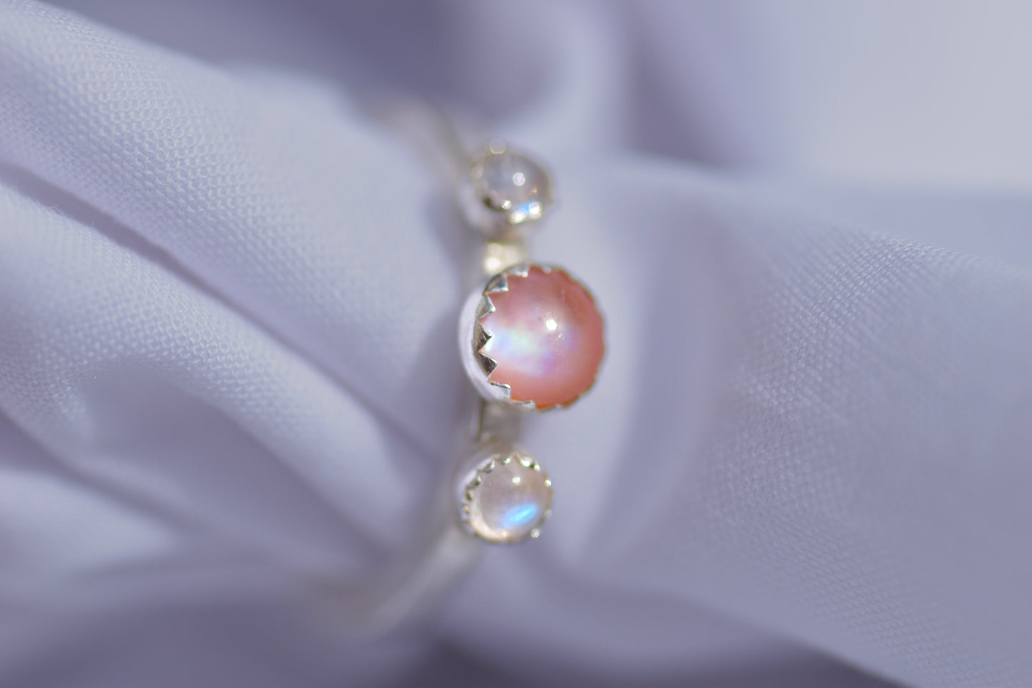 three stone silver ring featuring pink mother of pearl and two blue moonstones 