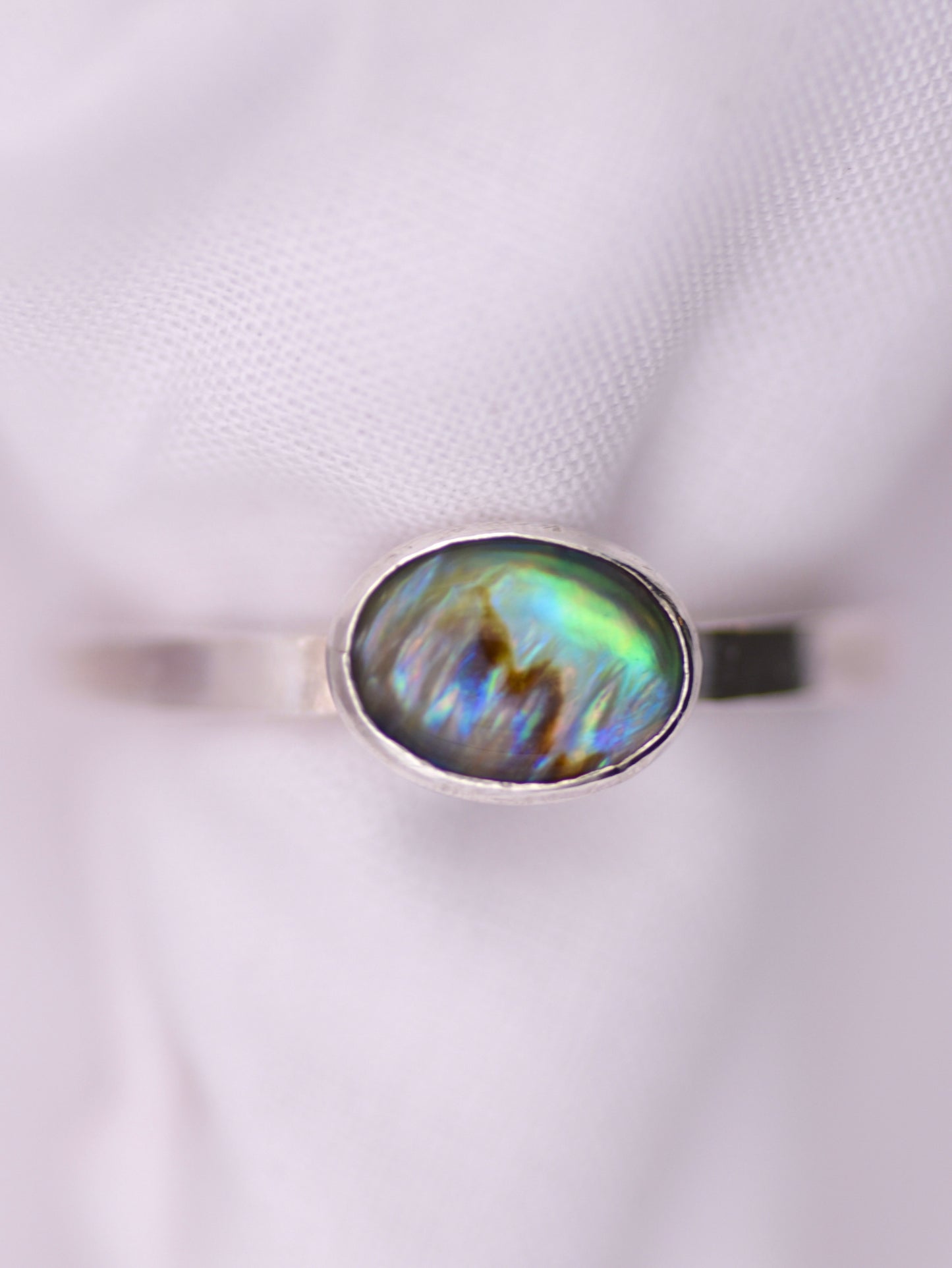 Silver ring with an oval paua shell on a white background