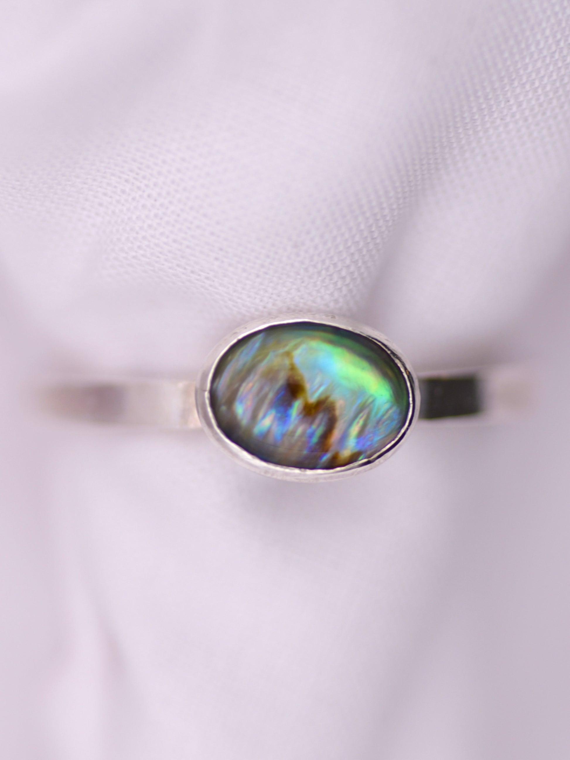 Silver ring with an oval paua shell on a white background