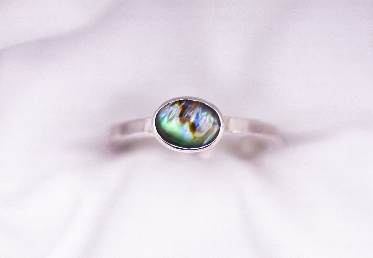 Silver ring with a paua shell gemstone on a white background