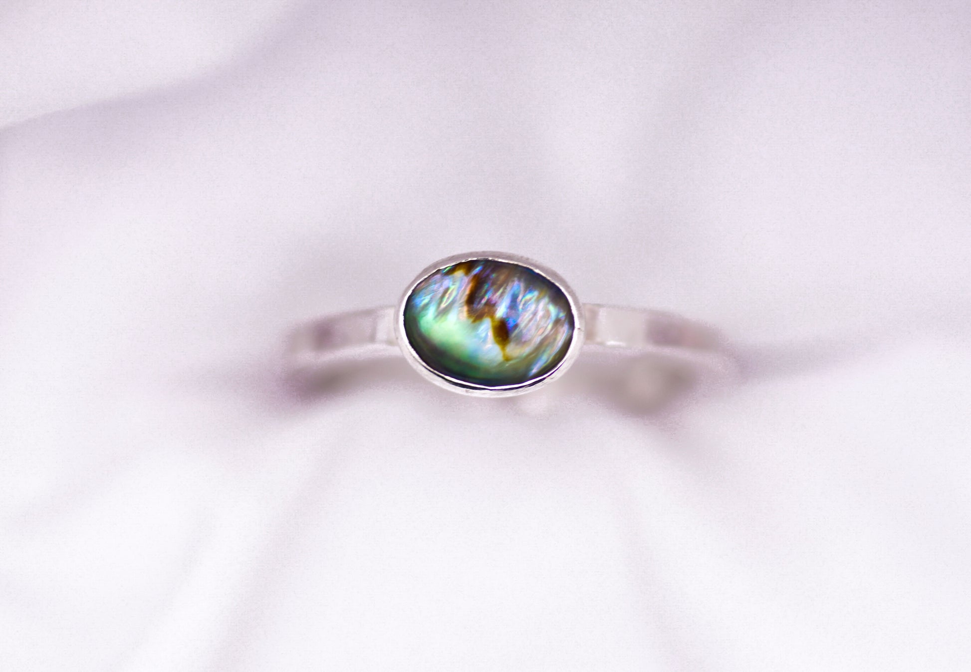 Silver ring with a paua shell gemstone on a white background