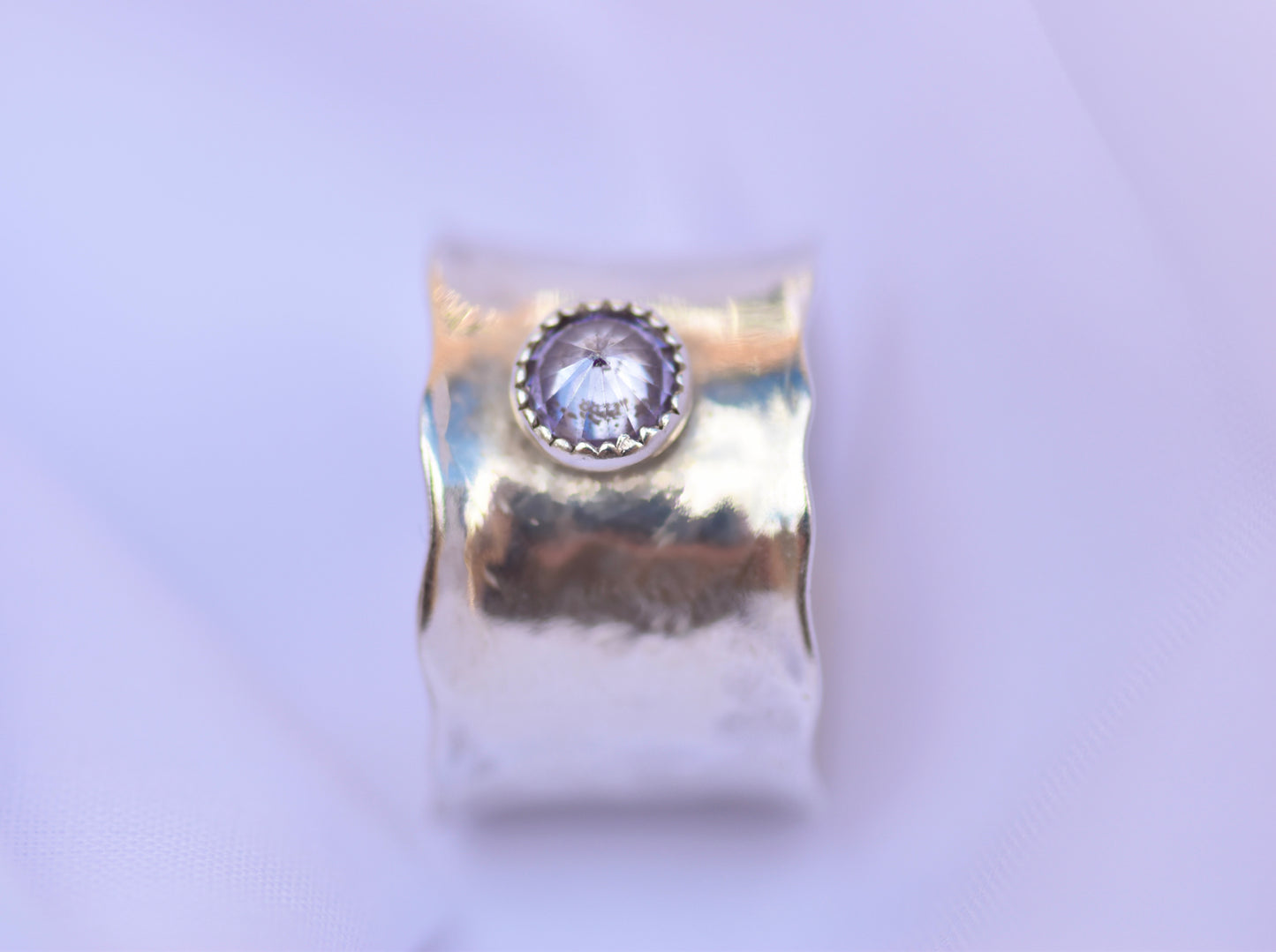 silver ring with a central gemstone on a light purple background