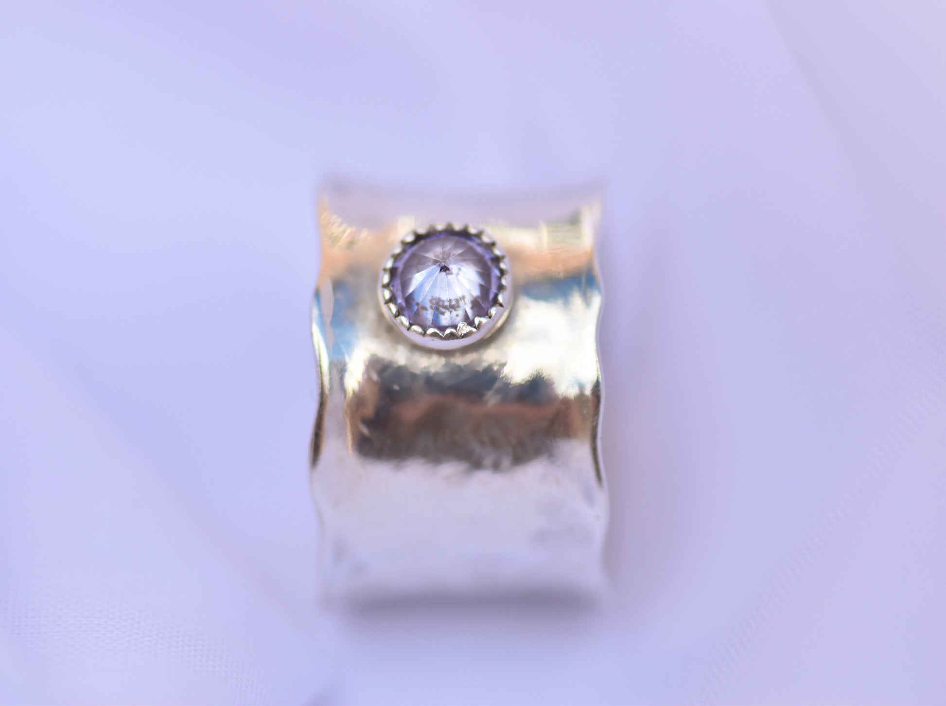silver ring with a central gemstone on a light purple background