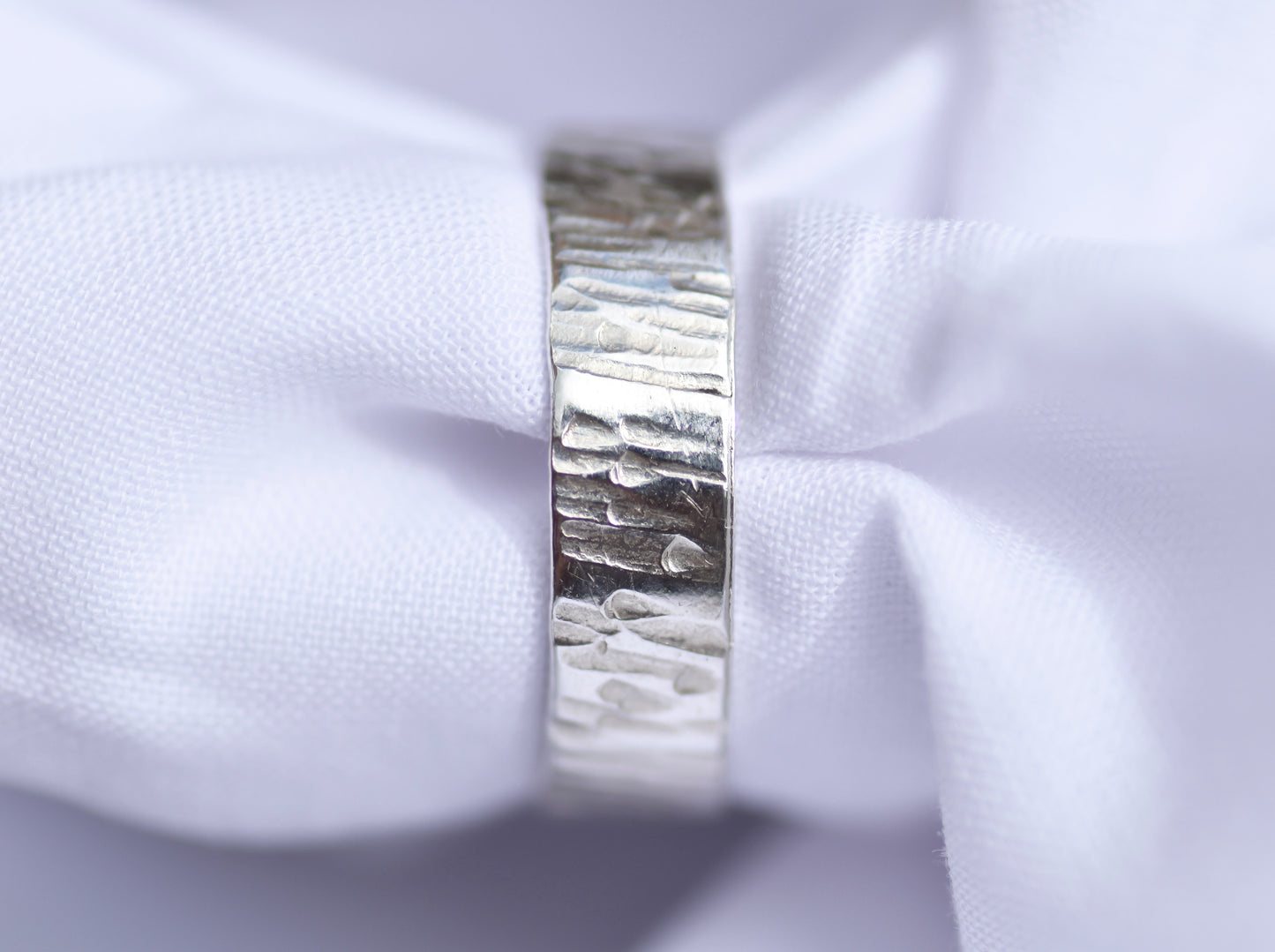 Close-up of a silver ring with a textured band on a white fabric background