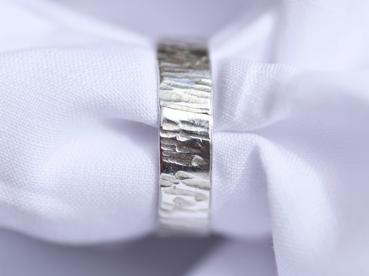 Close-up of a silver ring with a textured band on a white fabric background