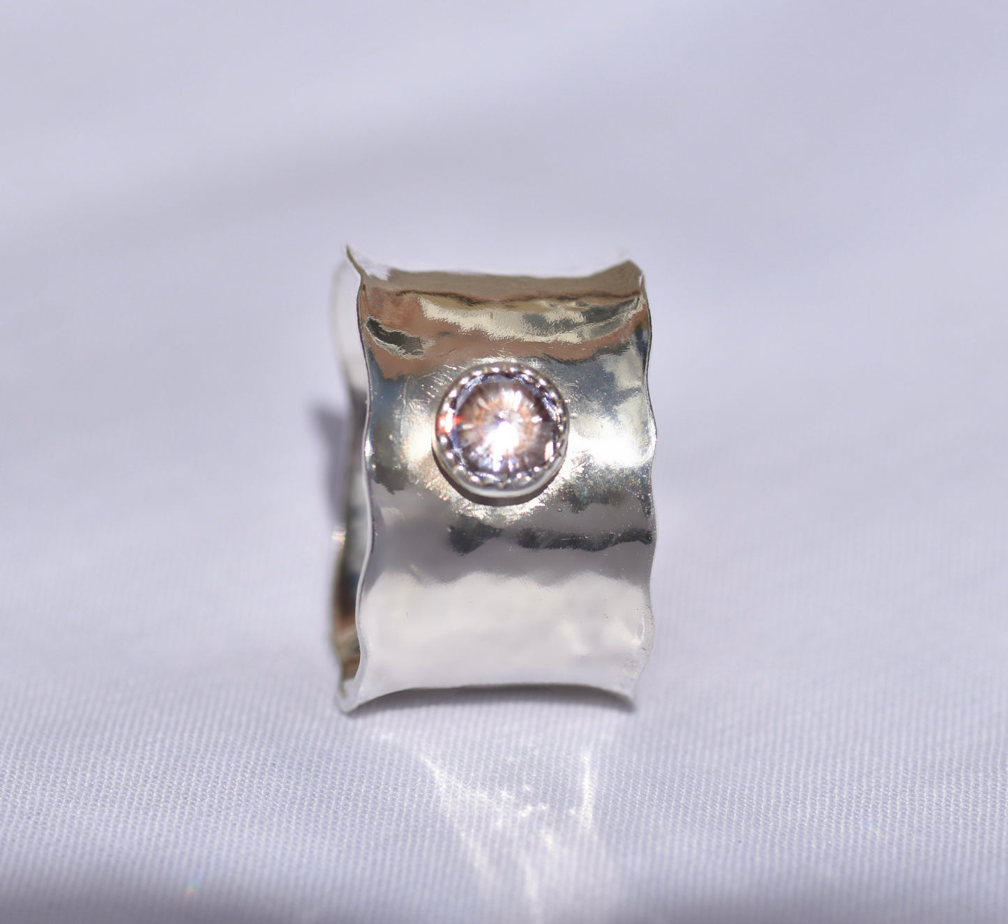 Silver ring with a central gemstone on a light gray background