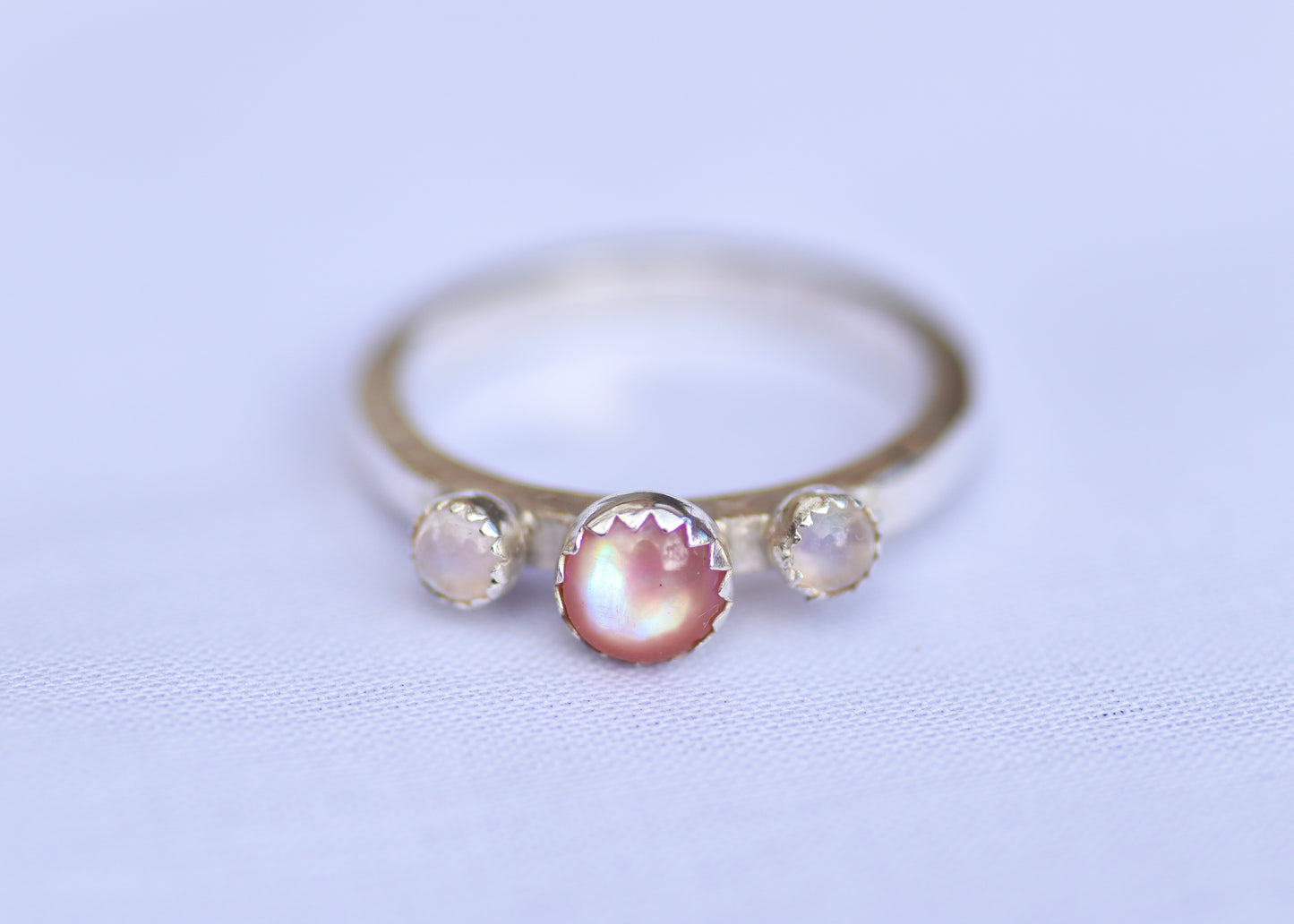 Silver ring with three gemstones on a light purple background