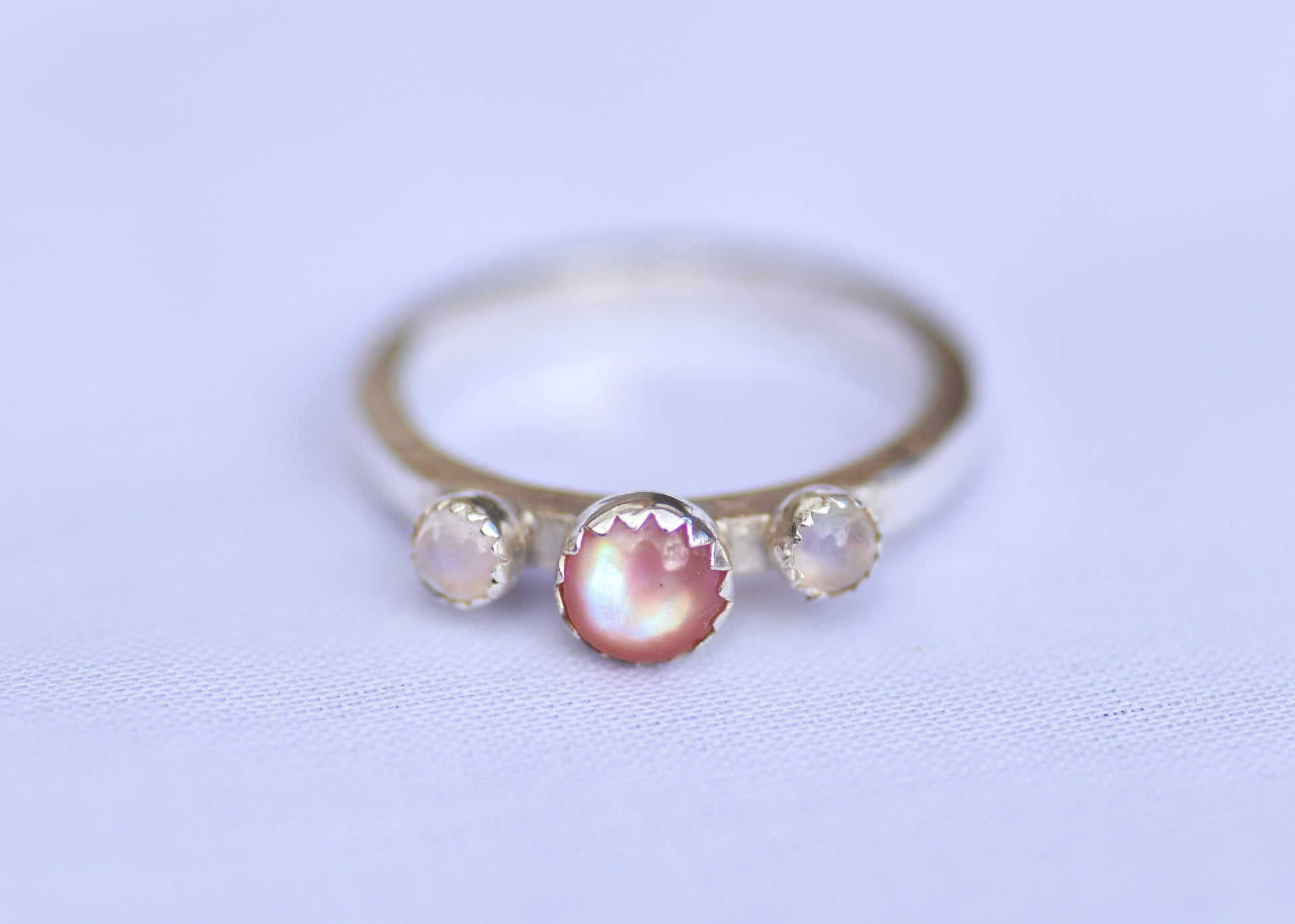 Silver ring with three gemstones on a light purple background