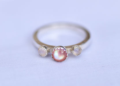 Silver ring with three gemstones on a light purple background