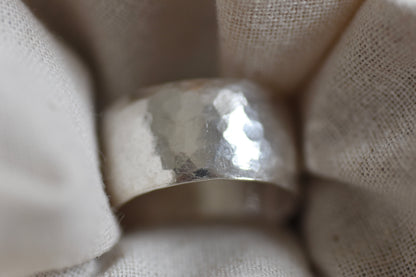 A hammered sterling silver band ring nestled in soft, textured off-white fabric.