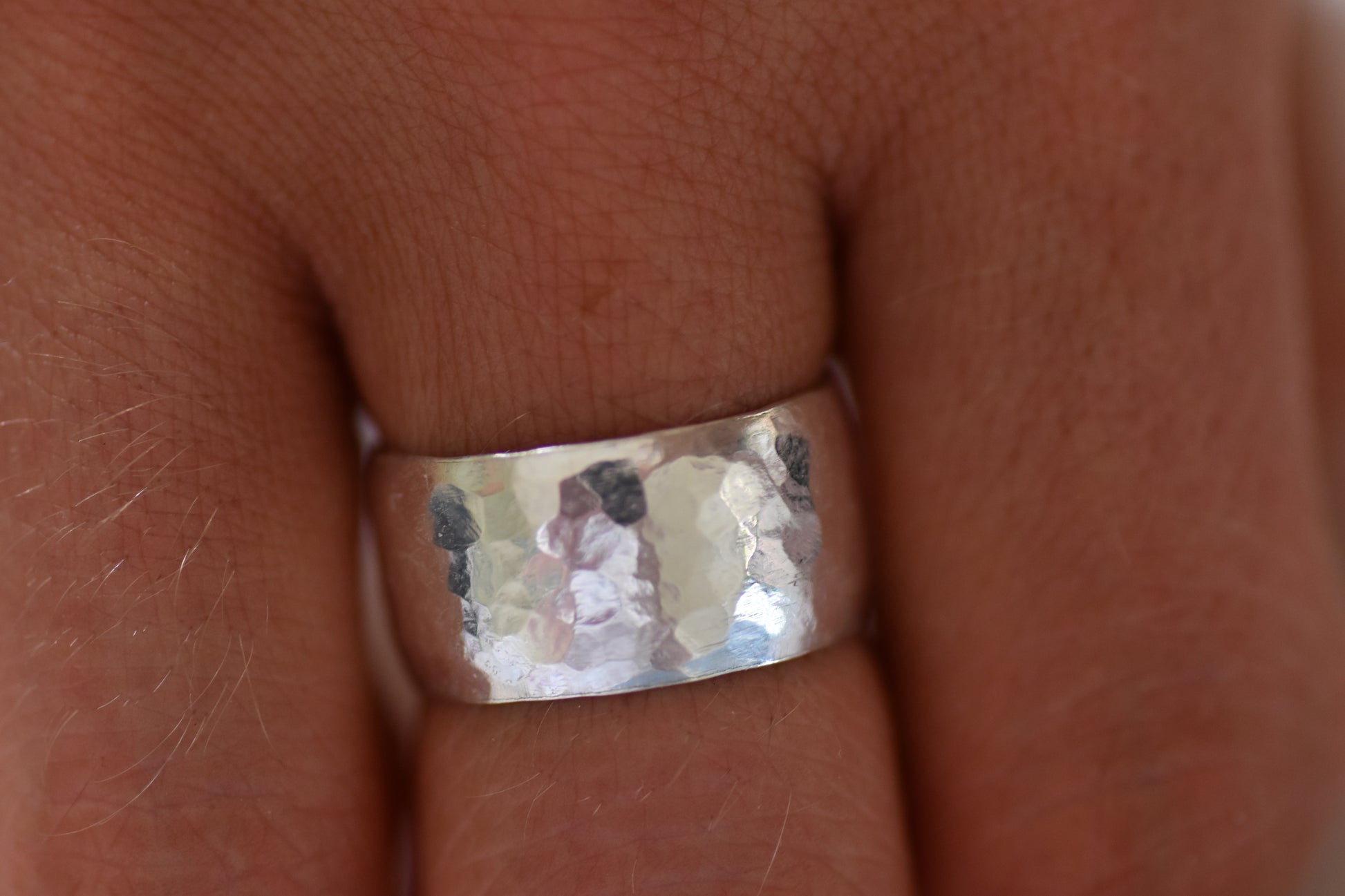 A hammered silver band ring worn on a finger, shown in a close-up shot against skin tones.
