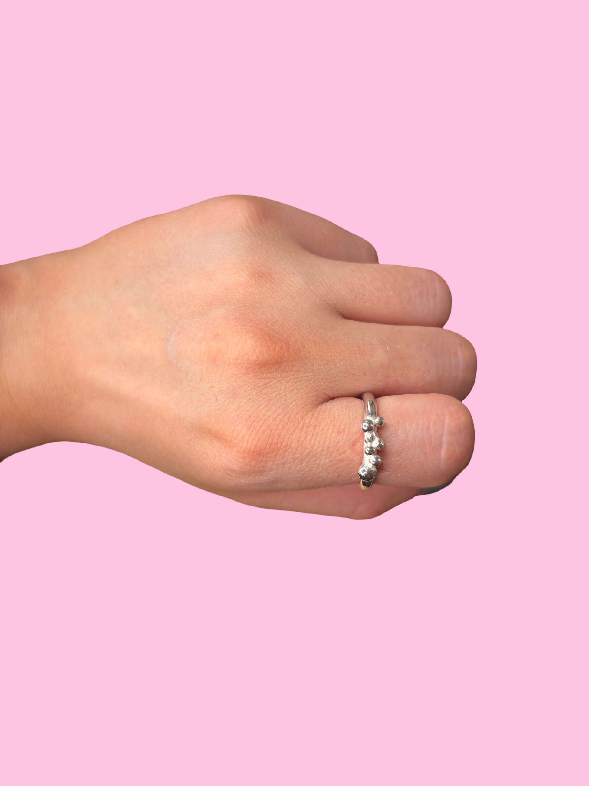 Hand wearing a silver ring on a pink background