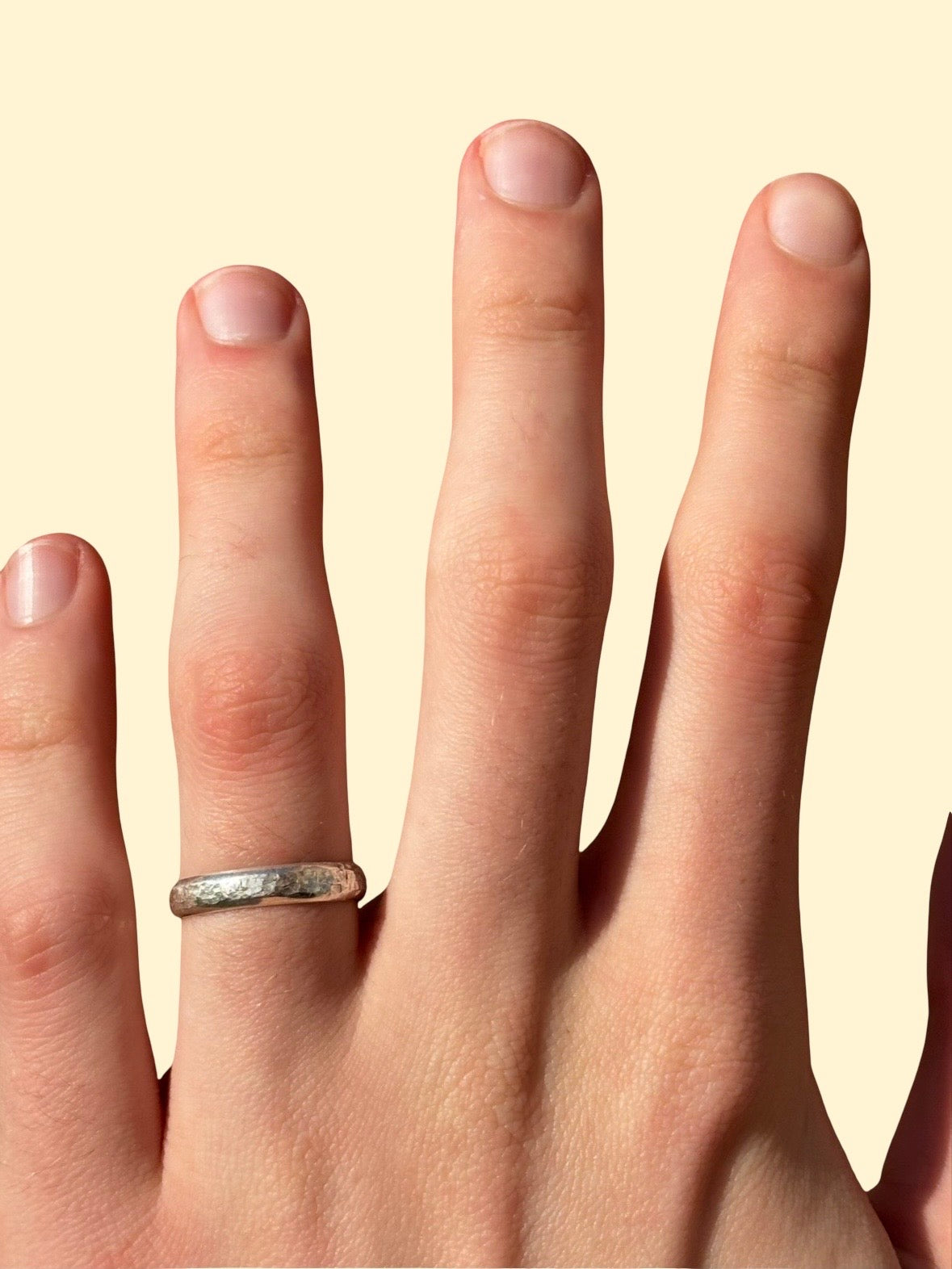 Hand wearing a silver ring on a beige background