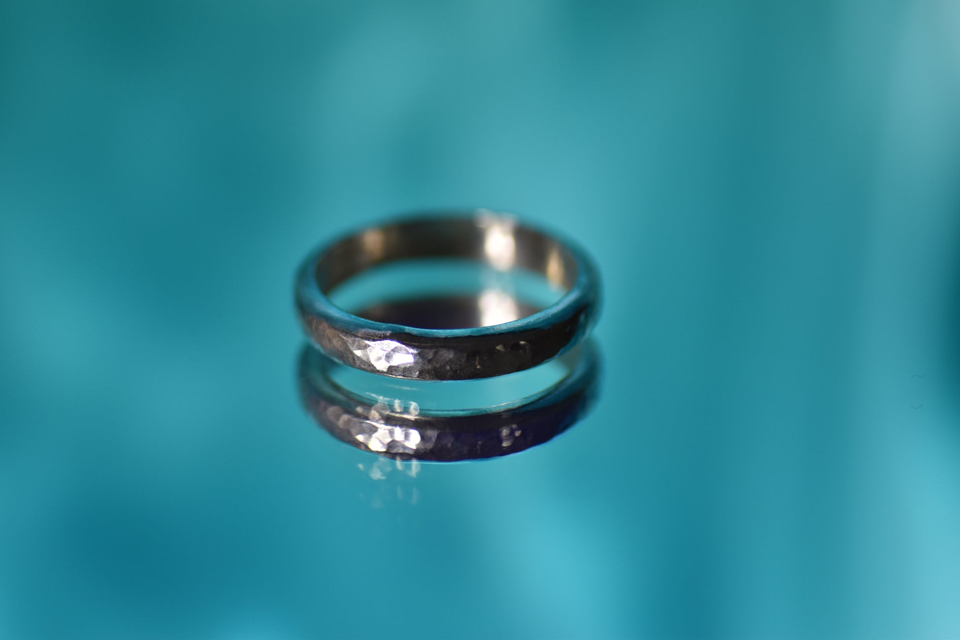 Silver ring on a reflective surface with a teal background