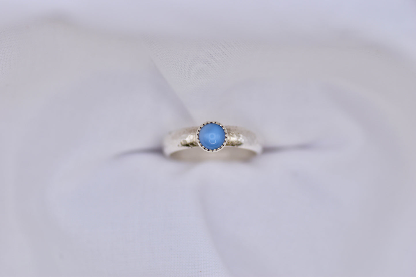 Silver ring with a blue gemstone on a light gray background