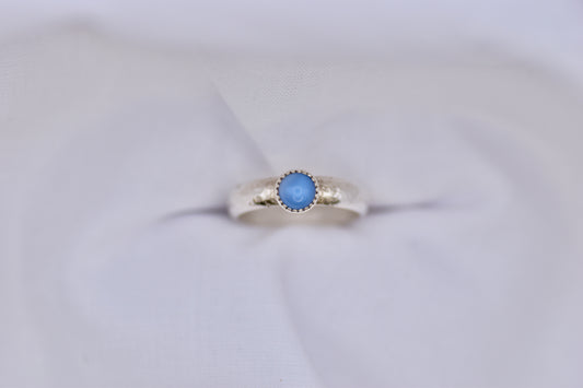 Silver ring with a blue gemstone on a light gray background