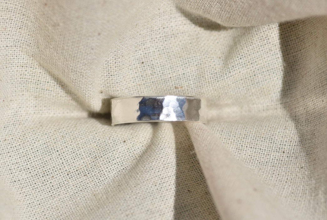 A hammered silver band ring resting on a textured beige linen fabric background.