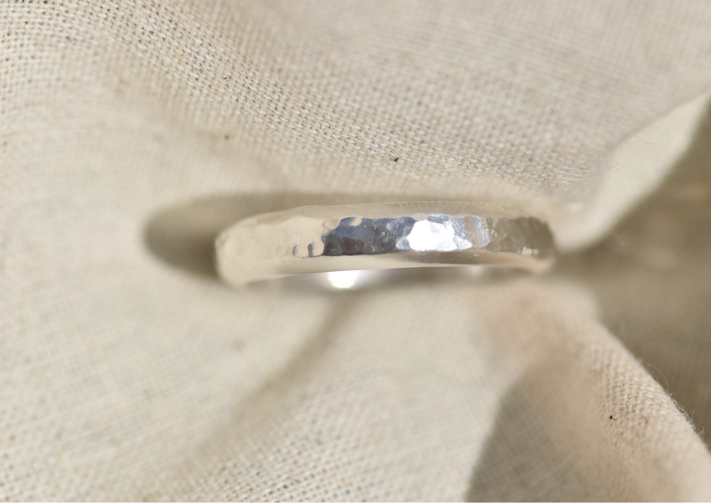 A hammered silver band ring displayed on a textured beige fabric stand.